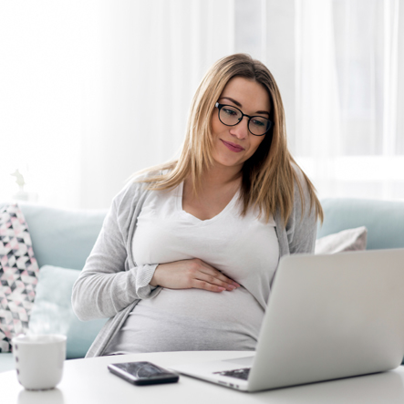 Zwangere vrouw met bril achter een laptop, bezig met het maken van het geboortekaartje