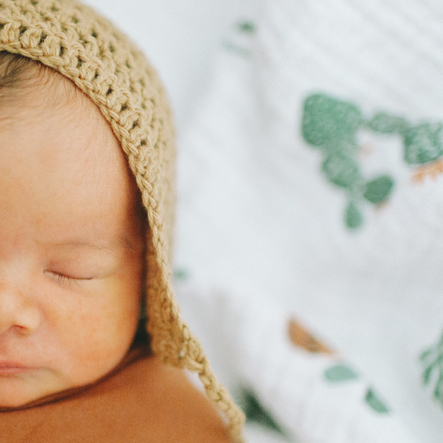 Een half portret van een newborn baby. De pasgeboren baby heeft een gehaakt mutsje op en ligt ingewikkeld in een terra-kleurige swaddle