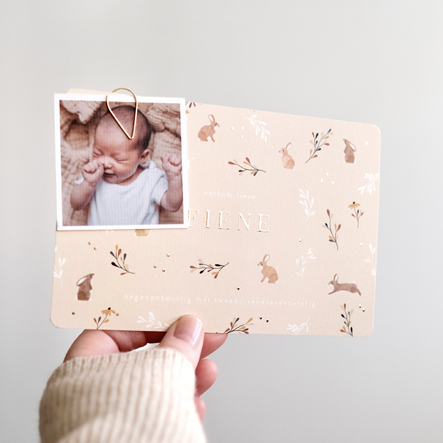 Zachtgeel geboortekaartje met haasjes, konijntjes, bloemen, takjes, goudfolie en een klein fotootje vastgemaakt aan het geboortekaartje met een druppel paperclip