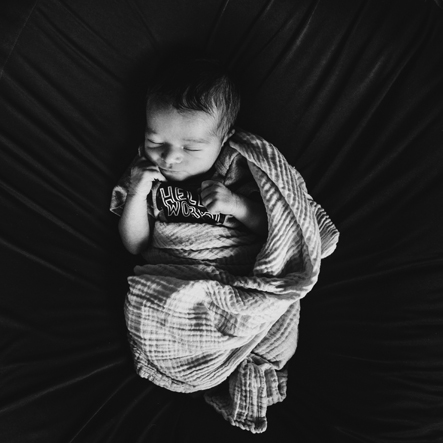 Zwart-wit foto van een newborn baby op een donker velours kussen