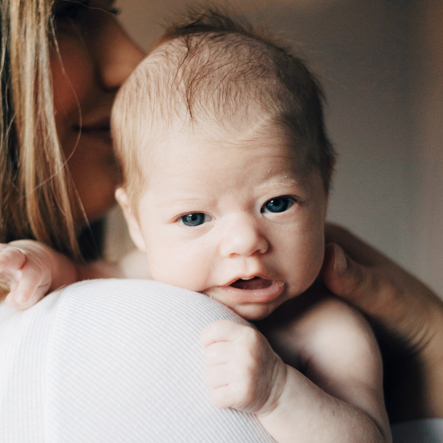 Newborn baby die je aankijkt over de schouder van zijn of haar moeder.